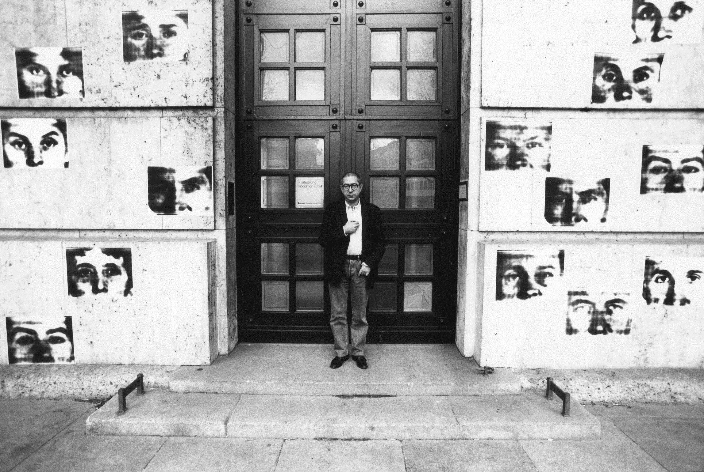 Ein Mann steht vor einer großen Tür. Mehrere Bilder hängen an der Wand um die Tür.