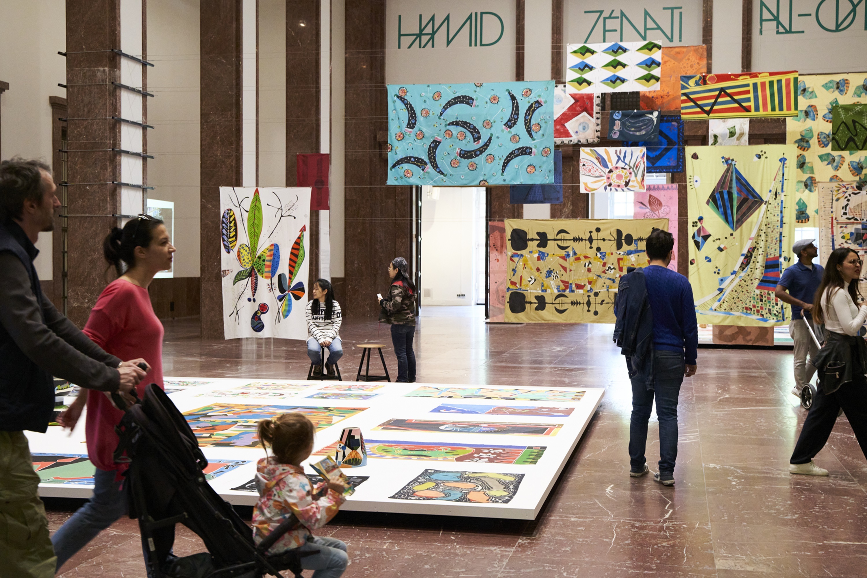 People in a museum hall, where printed cloths are hanging.