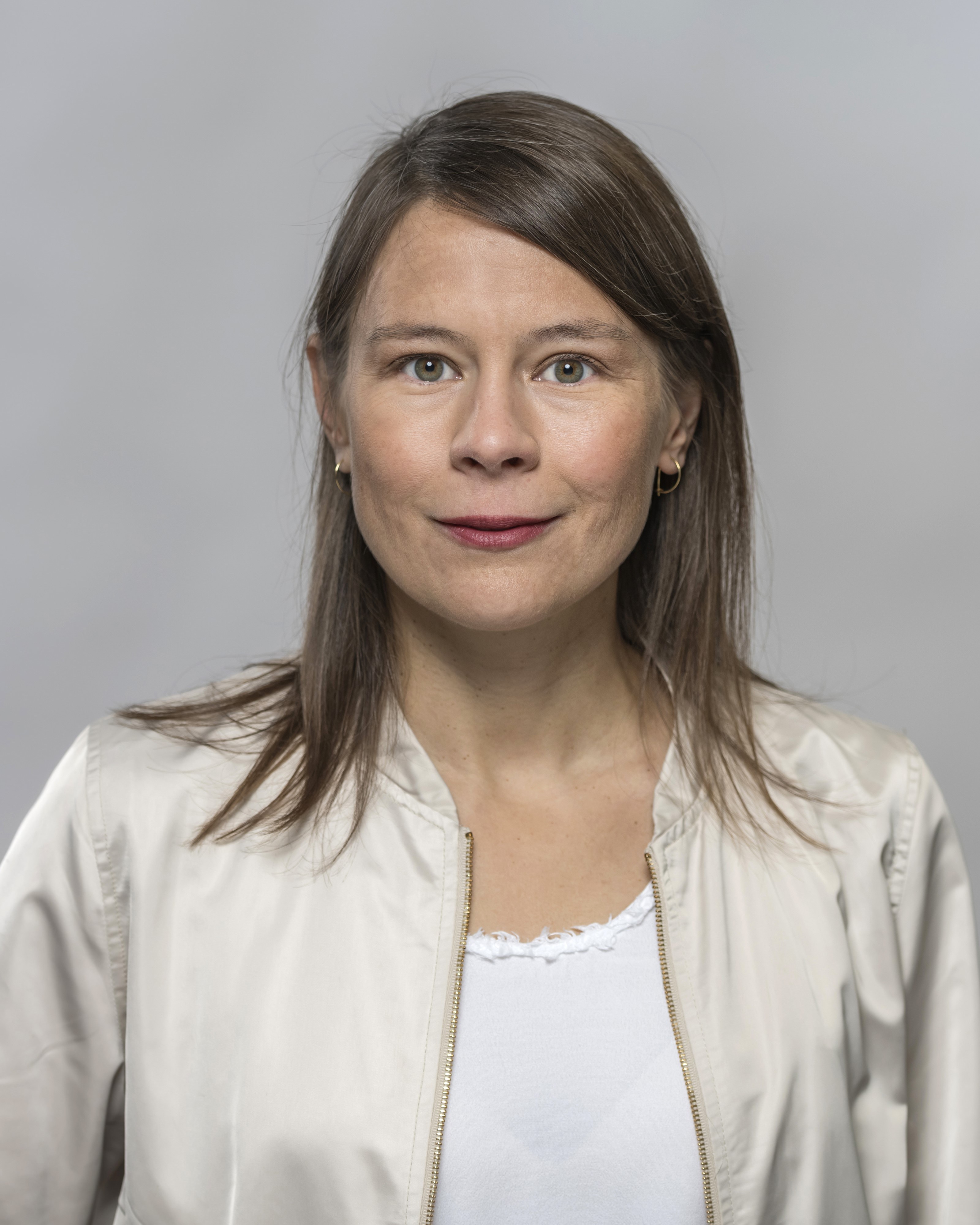 A woman with brown, straight hair. She is wearing a white jacket.