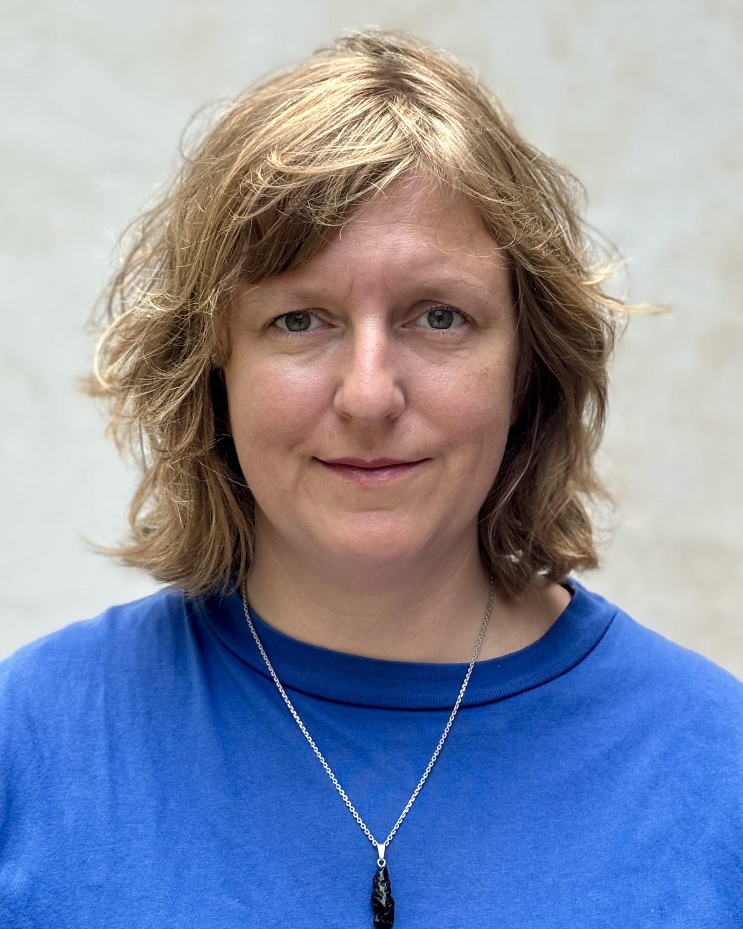 A woman with blonde, shoulder-length hair. She is wearing a blue top.