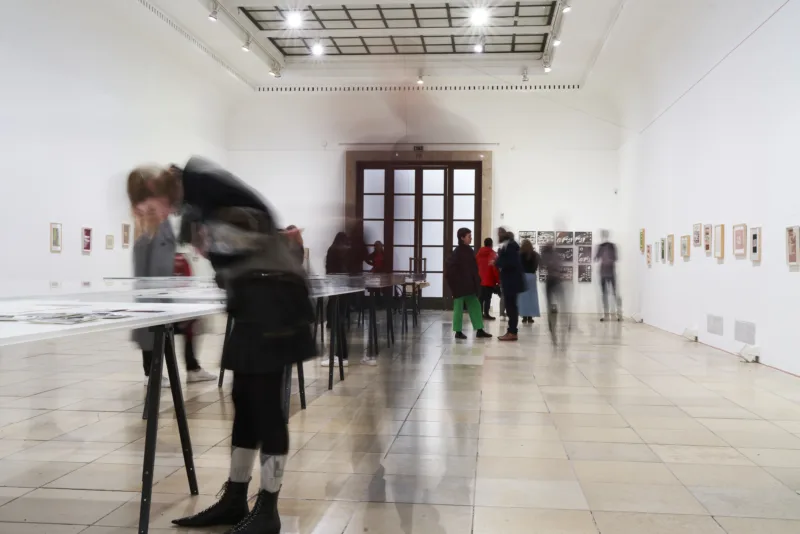 Viele Menschen in einem Ausstellungsraum mit Vitrinen und Bildern an den Wänden.