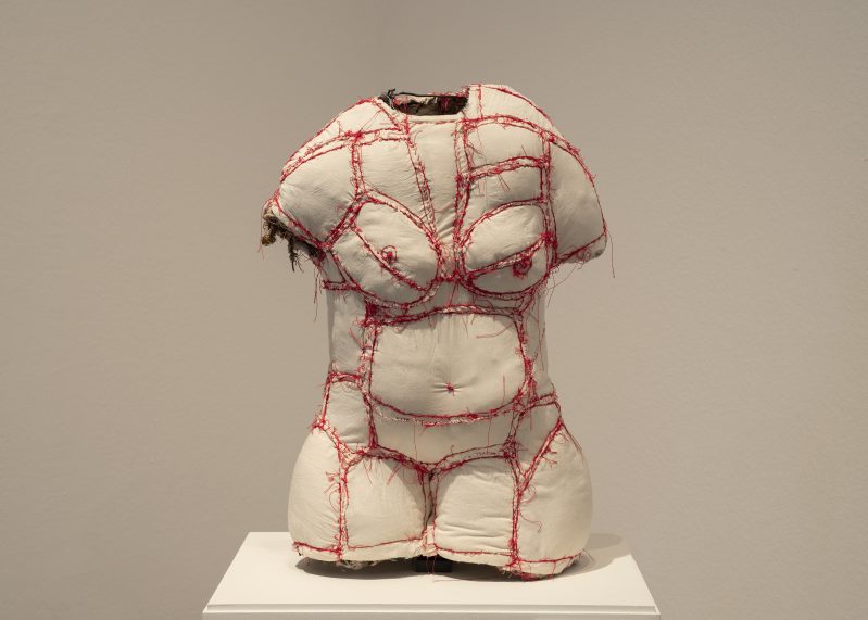 Eine Skulptur in Form eines weiblichen Torsos aus weißem Stoff mit roten Umrissen.