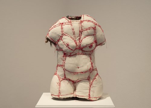 A sculpture in the shape of a female torso made of white fabric with red outlines.