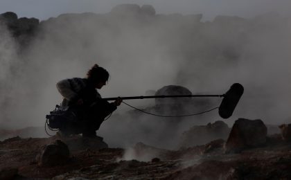 Eine Frau mit einem Mikrofon an einer steinigen Küste, umgeben von Nebel