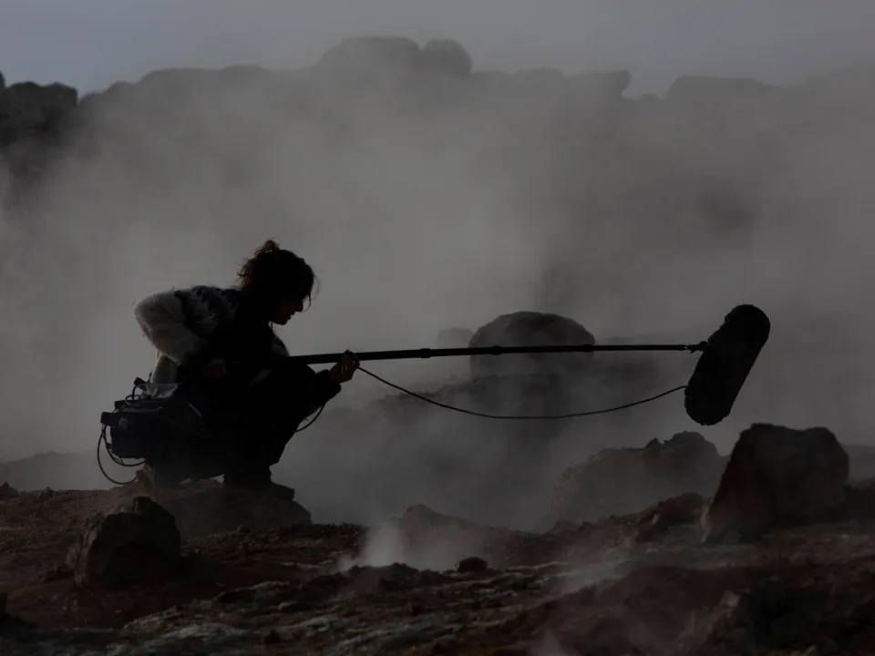 Eine Frau mit einem Mikrofon an einer steinigen Küste, umgeben von Nebel